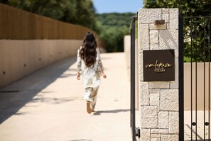 A person walking towards a stone wall with a sign that reads 'Villas.' - Valerozo Villa Maestosa - Pool, Jacuzzi & steps to the beach (Ionian Islands, Zakynthos)