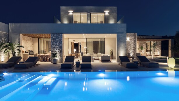 Una casa moderna de dos pisos con piscina, mobiliario exterior e interiores bien iluminados.