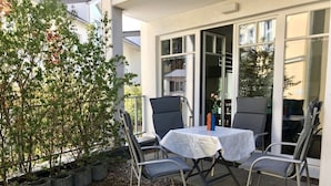 An outdoor patio with a table and four chairs, surrounded by potted plants and a small tree. - Villa Granitz Apartment (Göhren)