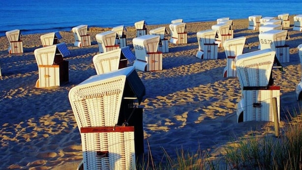 A beach with rows of white beach chairs with red straps, arranged in a pattern, facing the ocean. - Villa Granitz Apartment (Göhren)
