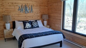 Un dormitorio de cabaña de madera con una cama, dos mesitas de noche y un ventanal grande.