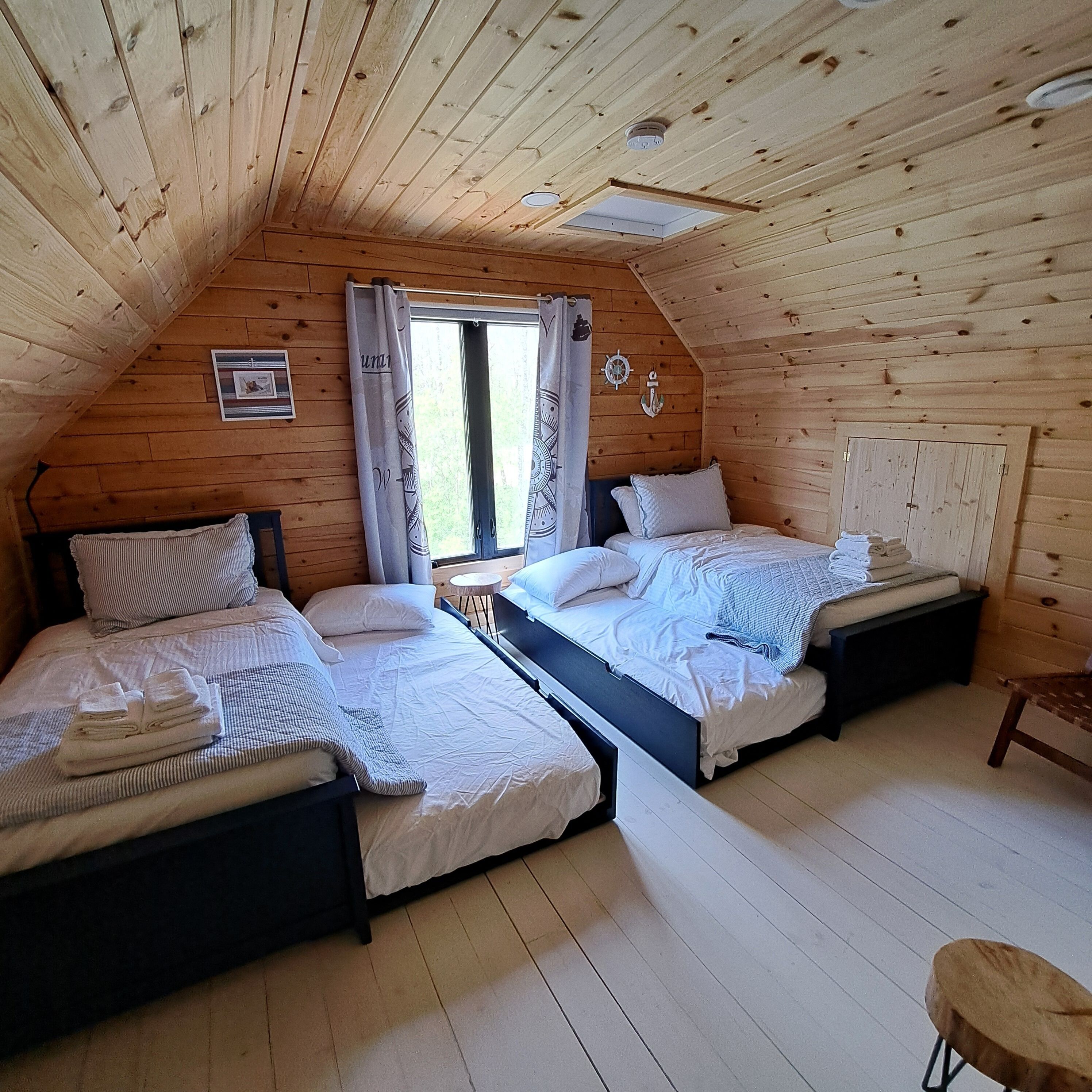 Una habitación acogedora tipo cabaña con dos camas, una mesita y una silla.