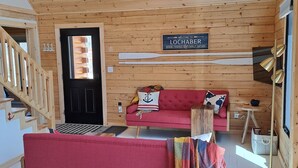 Interior acogedor de una cabaña con un sofá rojo, paredes de madera, un letrero de bienvenida y una escalera.