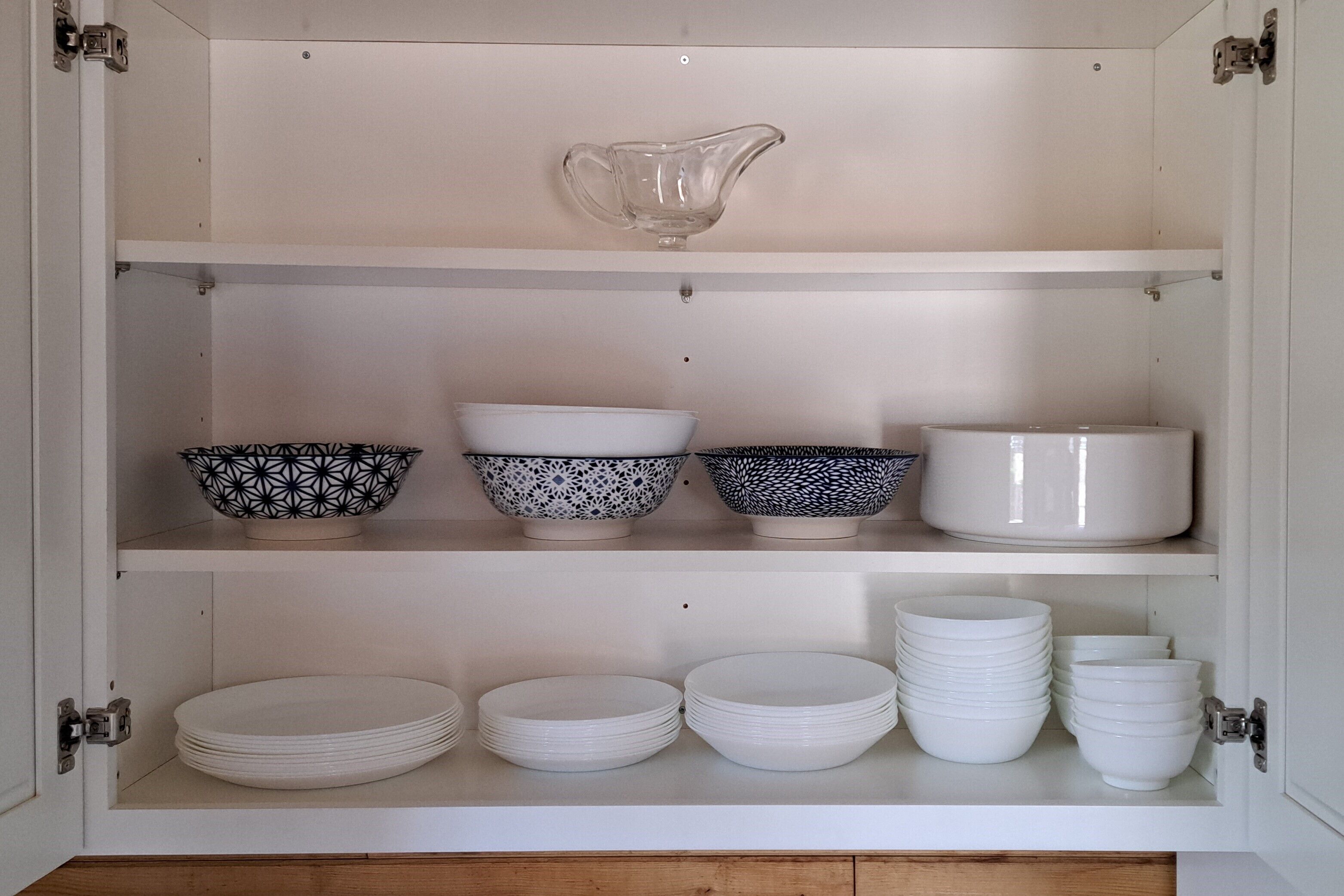A cabinet with shelves containing bowls, plates, and a pitcher.
