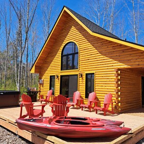 Eine Blockhütte mit einer Veranda, roten Adirondack-Stühlen und einem roten Kanu.