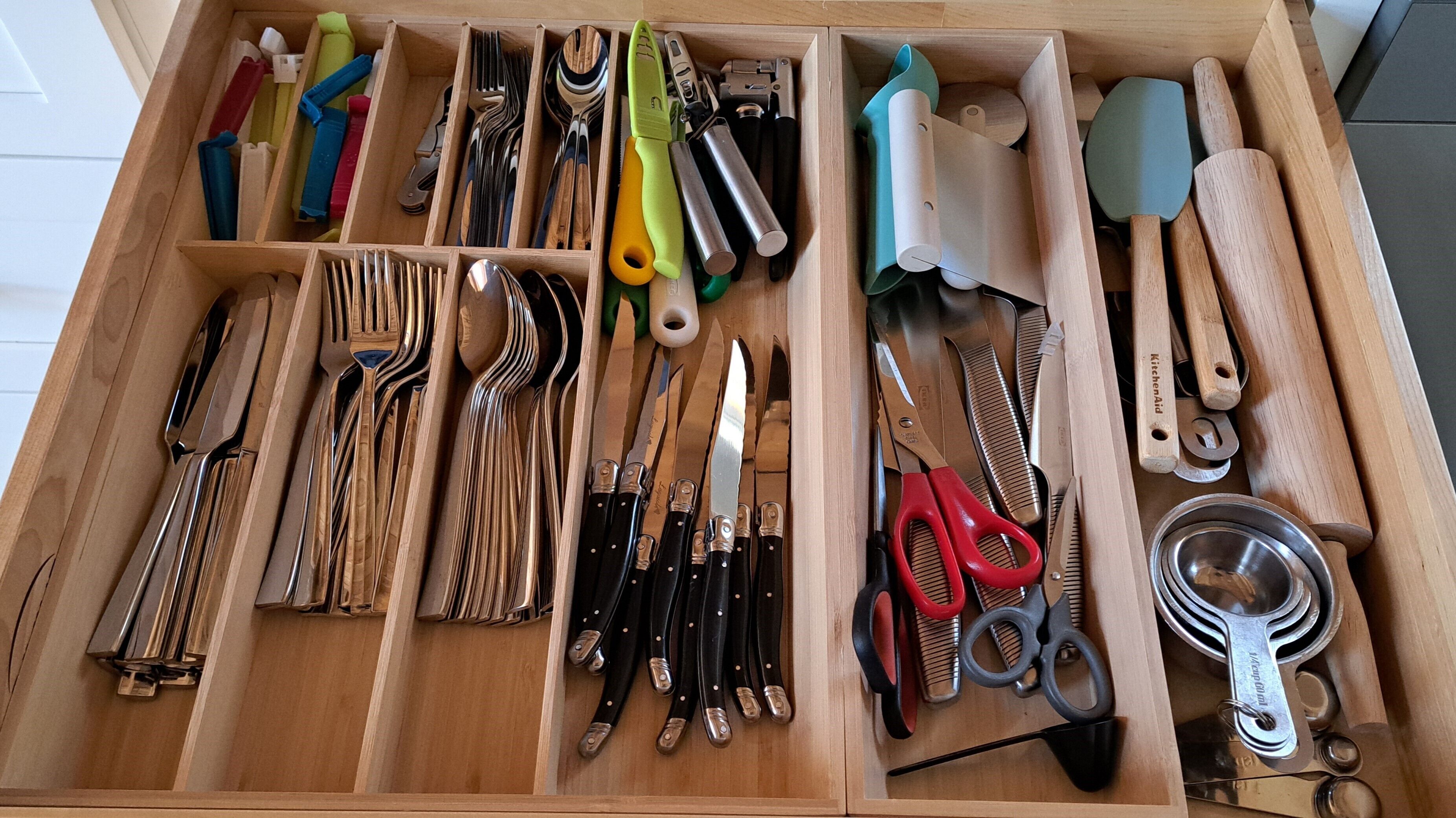 Un tiroir rempli de divers ustensiles et outils de cuisine, notamment des couteaux, des ciseaux et des instruments de mesure.
