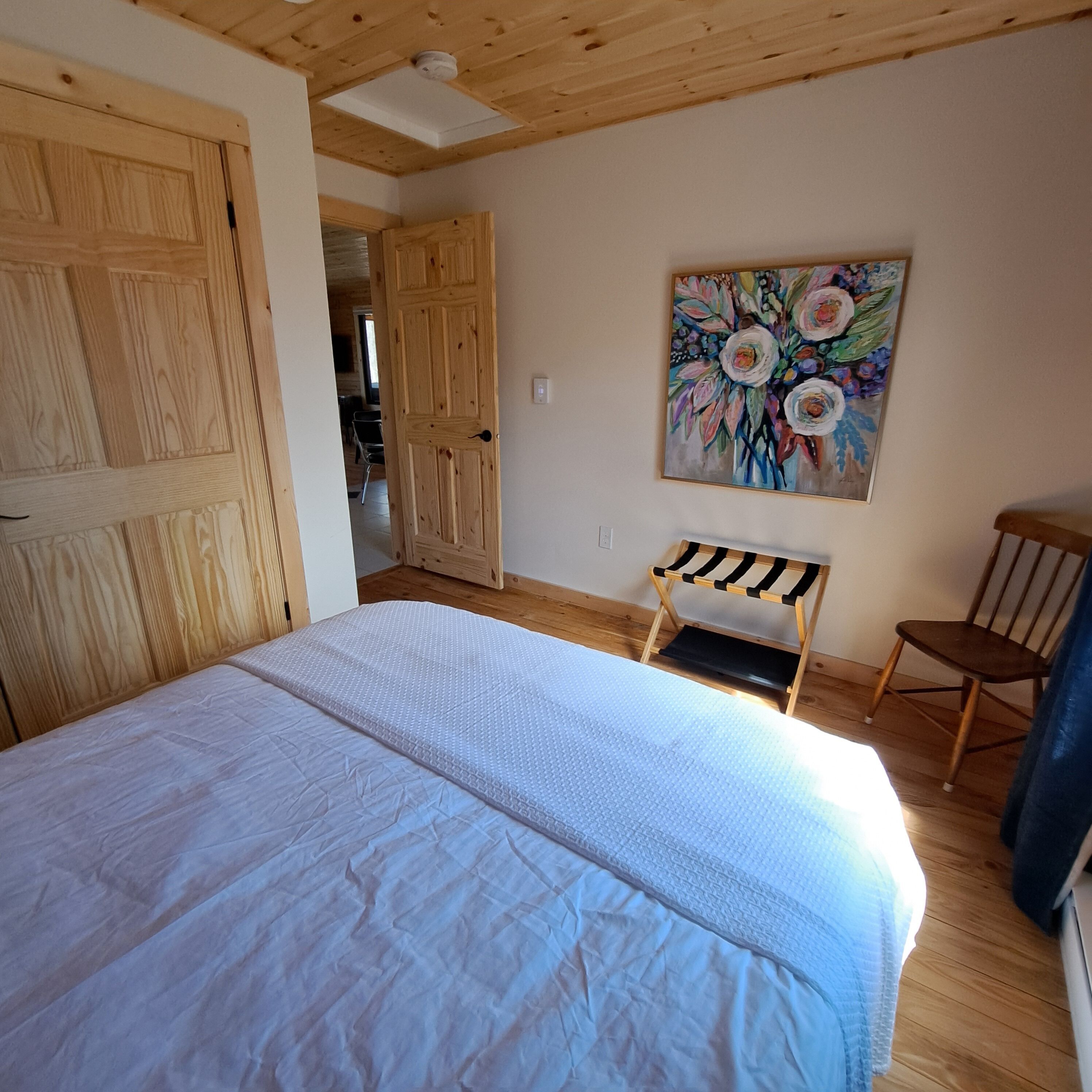 A bedroom with a large bed, wooden walls, a painting, and a bench.