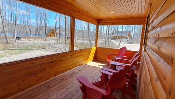 Eine Holzhütte mit großen Fenstern, roten Adirondack-Stühlen und Blick auf See und Wald.