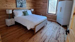 Een houten slaapkamer met een bed, nachtkastjes, een kledingkast en een raam.