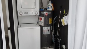 Un lavadero pequeño con lavadora y secadora, una cesta de ropa, productos de limpieza y una aspiradora.