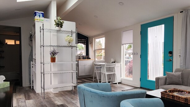 Una cocina moderna con armarios blancos, un comedor con sofá azul y una puerta verde azulada.