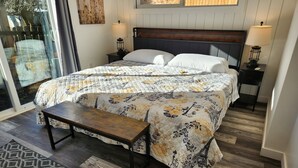 Un dormitorio con una cama grande, dos mesitas de noche con lámparas, un banco de madera y una alfombra estampada.