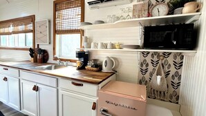 A compact kitchen with white cabinets, a sink, a coffee maker, and a microwave. - Tiny House - Big Fun! (Zanesfield)