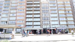A multi-story residential building with balconies and a ground-level commercial area with shops and outdoor seating. - Apartment in Nieuwpoort With sea View (Nieuwpoort)