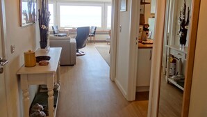 A hallway leading to a living area with a sofa, chairs, and a table with a vase of flowers. There are framed pictures on the walls and a mirror reflecting the room. - Apartment in Nieuwpoort With sea View (Nieuwpoort)