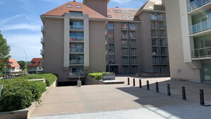 A multi-story residential building with balconies, a paved entrance area, and a clear sky. - Apartment in Nieuwpoort Near the Beach (Nieuwpoort)