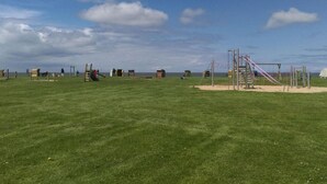 A grassy park with playground equipment and a clear sky. - North Sea Holiday House Wellmeyer (Wurster Nordseeküste)