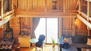L’intérieur d’un chalet rustique, avec un poêle à bois, un canapé, une table à manger et un balcon offrant une vue imprenable.