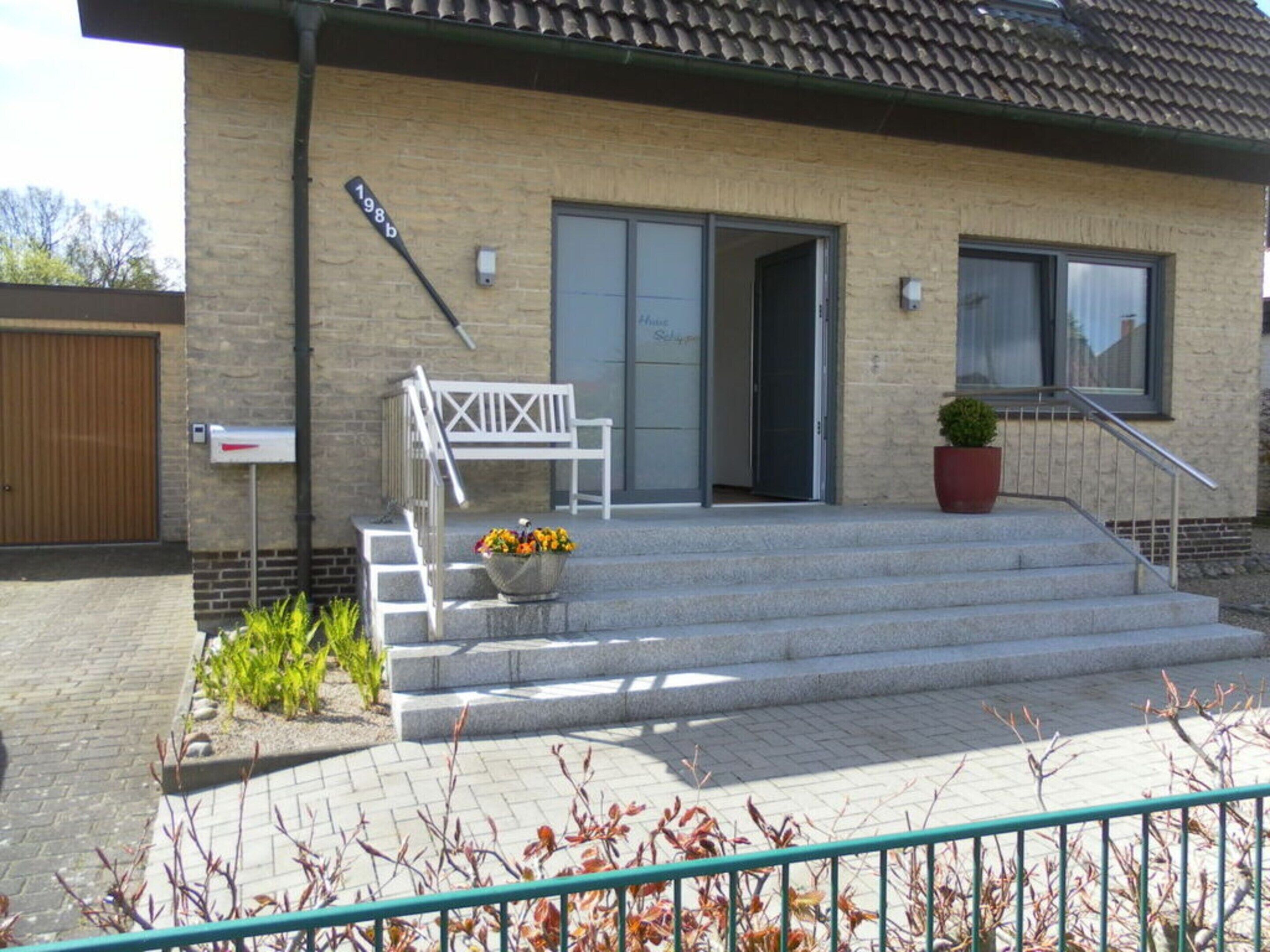 A building with a brick facade, a wooden door, a white bench, and a flower pot on the steps.