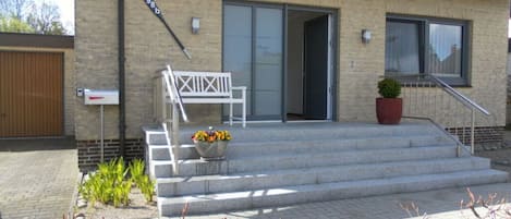 A building with a brick facade, a wooden door, a white bench, and a flower pot on the steps.
