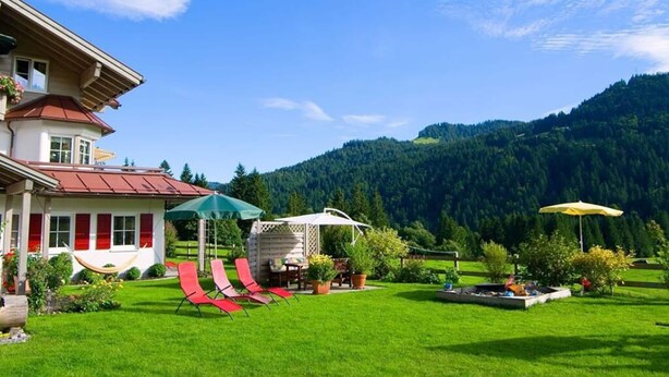 A house with a red-roofed building, a green umbrella, and a white gazebo in a lush green yard with a mountain backdrop. - 2 in Alpenrosle Modern Retreat (Balderschwang)