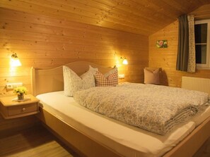 A cozy wooden cabin bedroom with a bed, nightstands, and wall-mounted lamps.