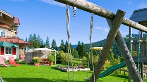 A wooden swing set in a backyard with a house, a covered patio, and a playground area. - 2 in Alpenrosle Modern Retreat (Balderschwang)