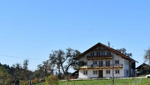 Ein zweistöckiges Haus mit einer symmetrischen Fassade, einem zentralen Eingang und einem sichtbaren Balkon im oberen Stockwerk.