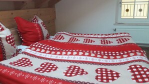 Ein Schlafzimmer mit schrägem Dach, einem Holz-Kopfteil und einem Fenster mit Gitterstäben.