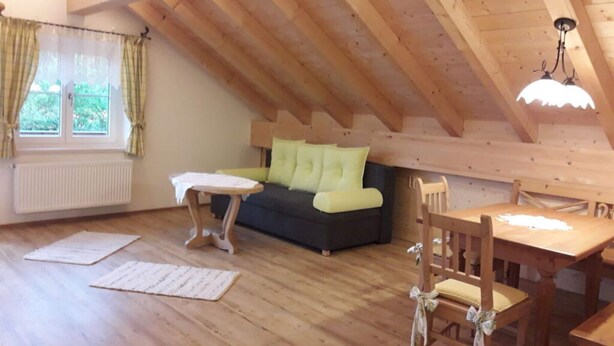 Ein gemütliches Dachzimmer mit Holzboden, einer Couch mit grünen Kissen, einem kleinen Tisch und einem Sessel.