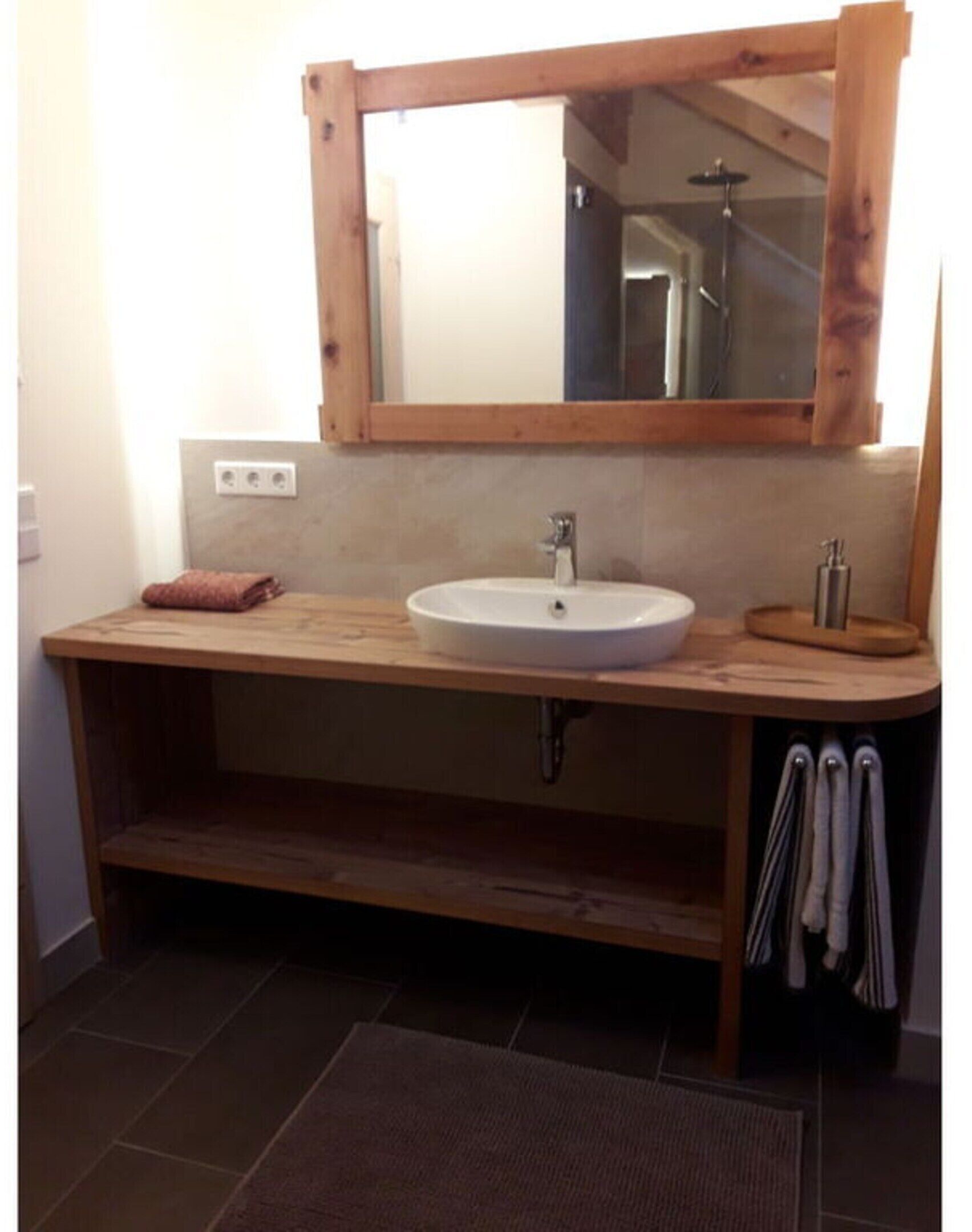 Un baño con tocador de madera, un lavabo blanco y un espejo encima. Hay un perchero y una toalla en la encimera.