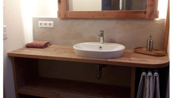 A bathroom with a wooden vanity, a white sink, and a mirror above it. There is a towel rack and a towel on the counter.