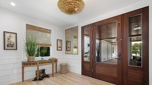 Une pièce avec un plancher en bois, une console en verre ornée d’une plante, un grand miroir et une porte en bois dotée d’une fenêtre.