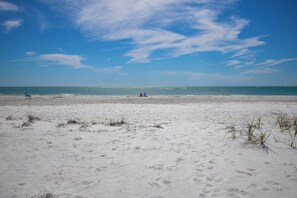 Una playa de arena blanca, cielo azul despejado y océano.