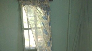 Una stanza con due letti, uno con copriletto a tema Winnie the Pooh e l'altro con copriletto bianco. Si vede una finestra con una tenda parzialmente tirata, e un tavolino con un oggetto blu sopra.