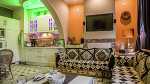 A living room with a sofa, a television, and a kitchen area with cabinets and a sink. - Very Nice Manor House in North African Atmosphere (Kortrijk)