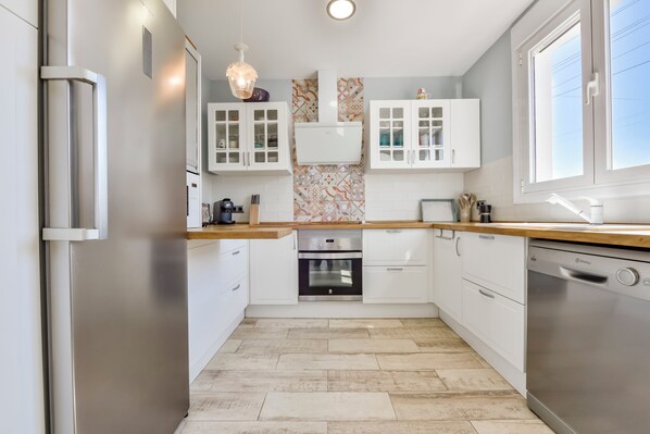 A modern kitchen with white cabinetry, a built-in oven, a dishwasher, and a window providing natural light.