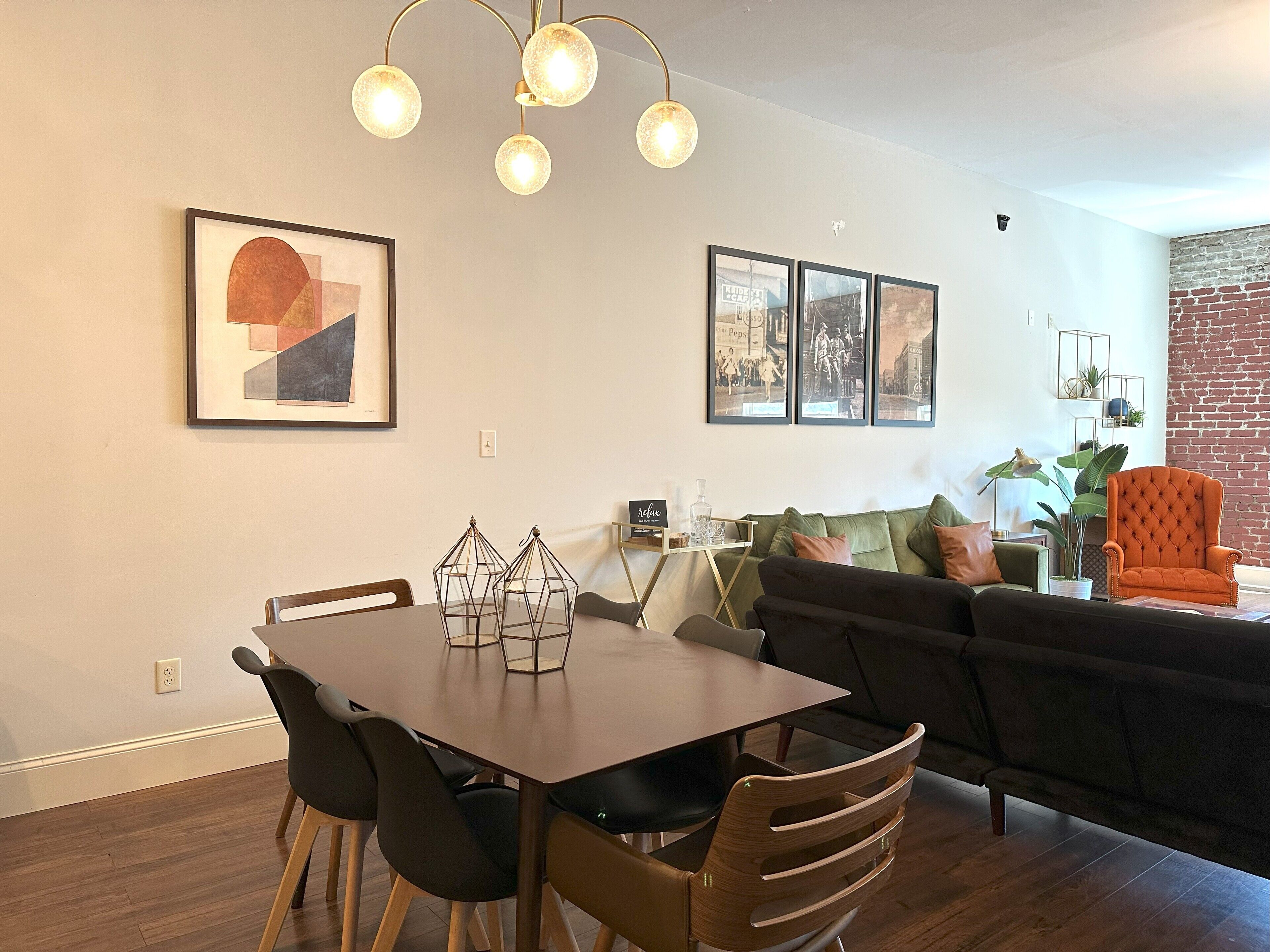 Una sala de estar moderna con comedor, que incluye un sofá oscuro, una mesa de comedor de madera y una araña.