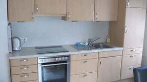 Een kleine keuken met houten kastjes, een roestvrijstalen spoelbak, een inbouwoven en een waterkoker.