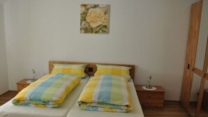 Een tweepersoonsbed met houten hoofdeinde, twee nachtkastjes met lampen, een enkel schilderij van een roos aan de muur en een houten garderobe.