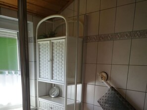 A bathroom with white tiled walls, a white cabinet with a clock, and a towel rack.