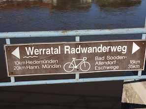A directional sign for a cycling route with distances to various destinations.
