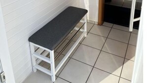 Een kleine, afgesloten ruimte met een bankje, een droogrek en een trap naar een hoger niveau.