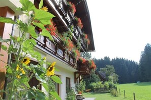 A traditional chalet with a balcony adorned with flowers and sunflowers, surrounded by a lush green landscape. - Child-friendly Apartment With Sauna (Hermagor-Pressegger See)