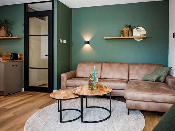 A modern living room with a brown leather sofa, two round coffee tables, and a light-colored rug.