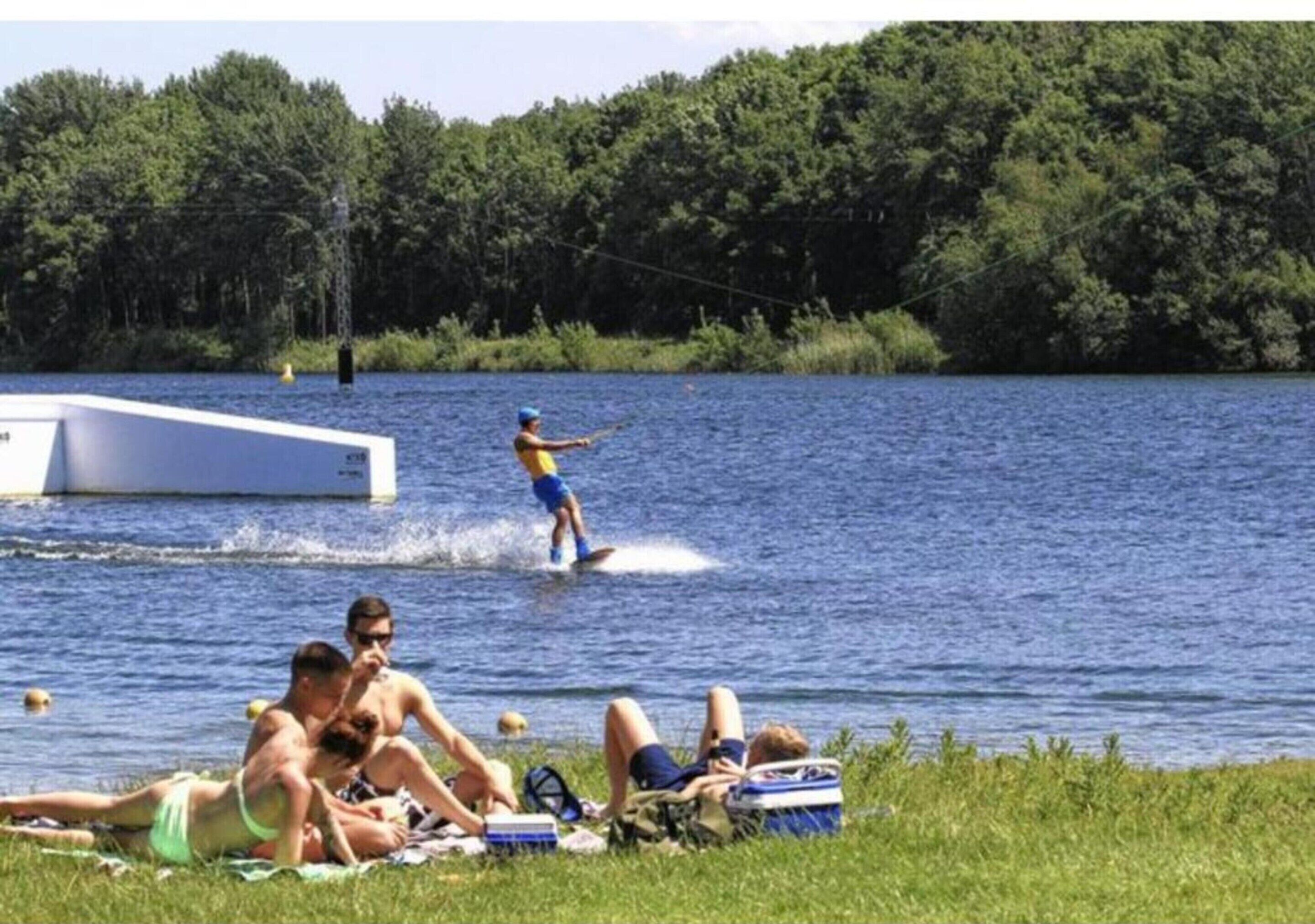 Eine Seenlandschaft mit badenden Personen und einem Wakeboarder.