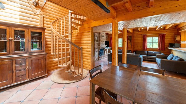 L’intérieur d’un chalet en bois comprend un escalier en colimaçon, un coin repas et un salon avec des canapés.