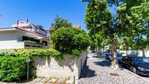 A residential street with a paved sidewalk, a white building with a red roof, and a tree-lined street. - Villino D'Agostino · Beachside 2-room villa flat, parking & 2 baths (Francavilla al mare)