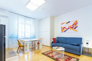 A modern living room with a blue sofa, a dining table with chairs, a coffee table, and a colorful abstract painting on the wall. - Villino D'Agostino · Beachside 2-room villa flat, parking & 2 baths (Francavilla al mare)