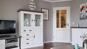 A living room with a TV, white cabinets, a sailboat decoration, and a door with a painting. - Kommodig Utkiek Modern Retreat (Zingst)
